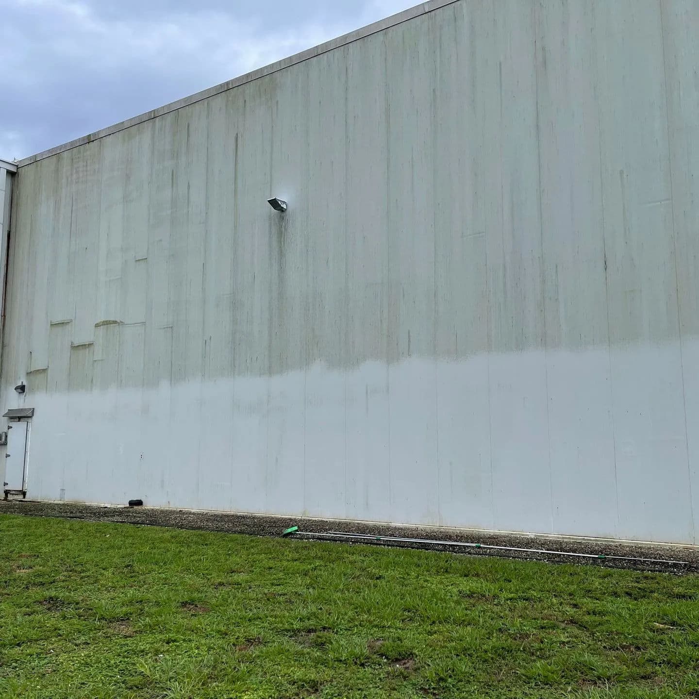 Dilapidated industrial wall with streaks, surrounded by green grass under a cloudy sky.