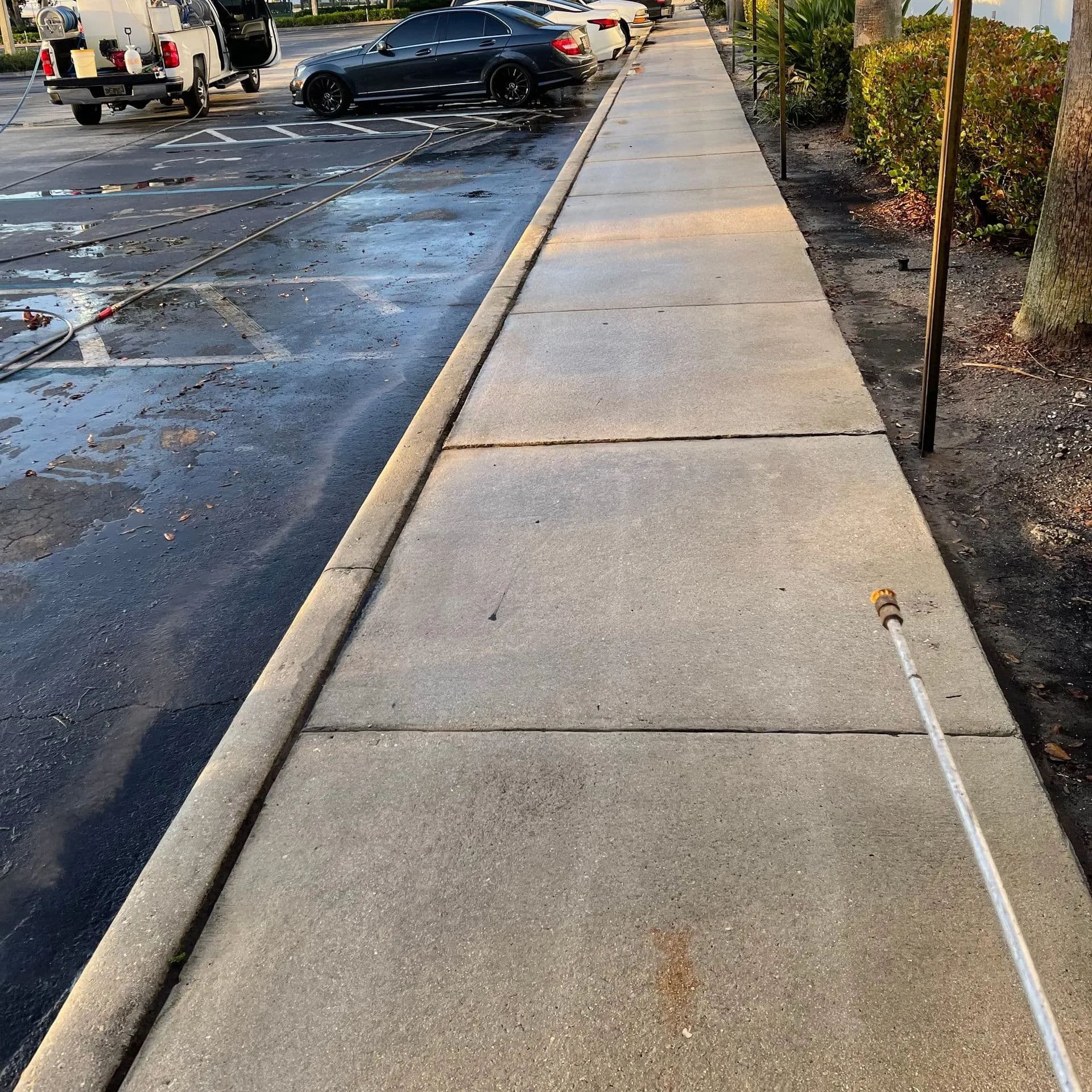 Sidewalk leading to a parking lot, with a car parked nearby and a pressure washer in view.